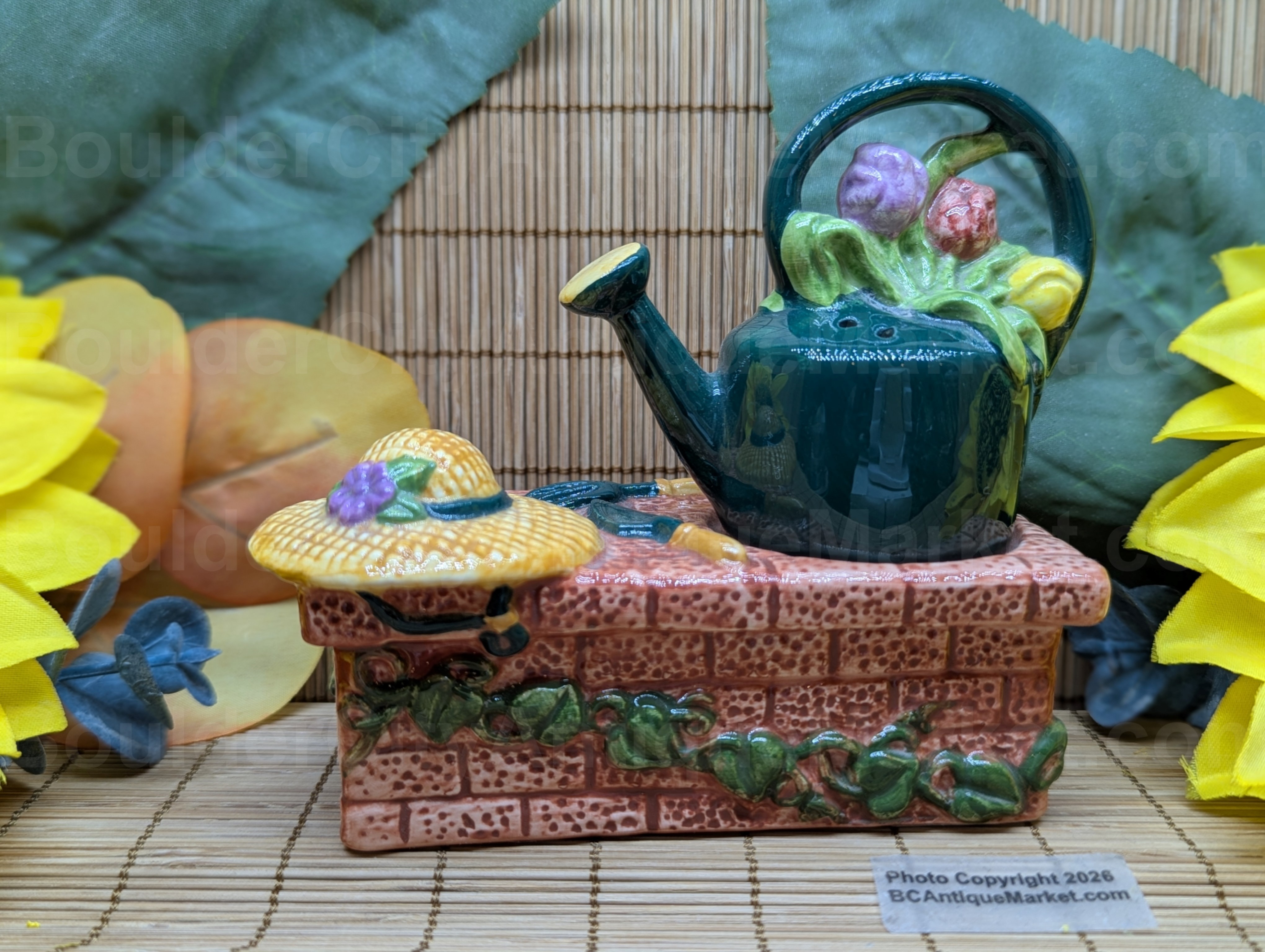 A straw hat on a vine wrapped garden bench, a couple tools, and a tulip filled water pitcher create a peaceful garden scene through this salt and pepper set. Set stands a little over three inches in height.
